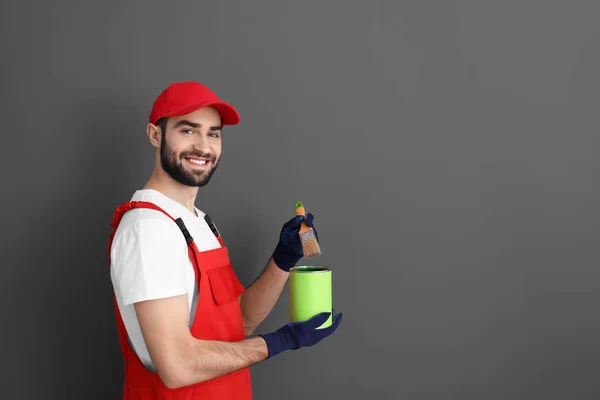 Masculino decorador segurando escova e pintura lata no fundo cinza — Fotografia de Stock