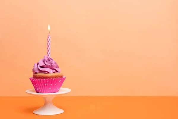 Birthday cupcake with candle on color background