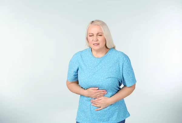 Woman suffering from abdominal pain on light background — Stock Photo, Image