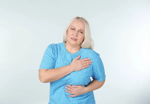 Woman suffering from chest pain on light background — Stock Photo, Image
