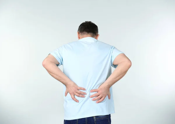 Man suffering from back pain on light background — Stock Photo, Image
