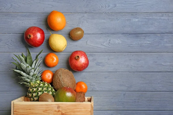 Crate and fresh tropical fruits on wooden background