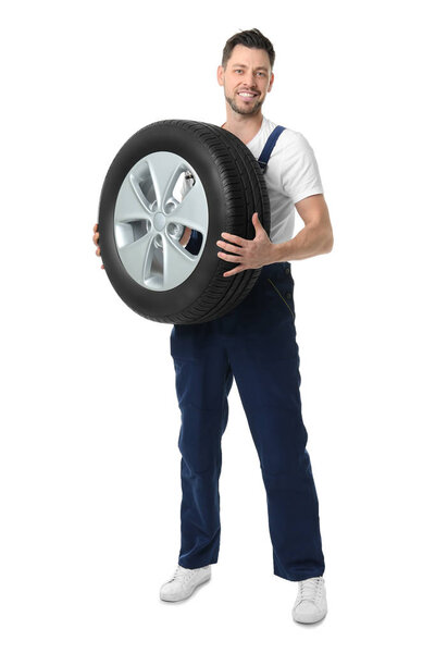 Male mechanic in uniform with car tire on white background