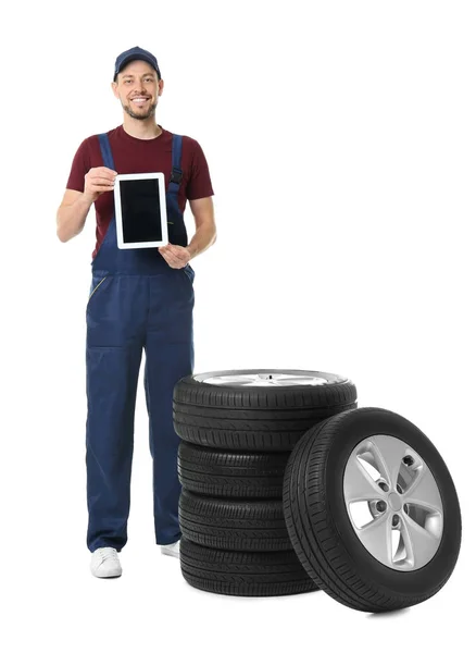 Mecânico masculino em uniforme com pneus de carro e tablet no fundo branco — Fotografia de Stock
