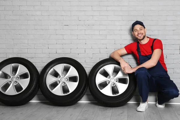 Araba lastikleri tuğla duvar arka plan ile üniformalı erkek makinist
