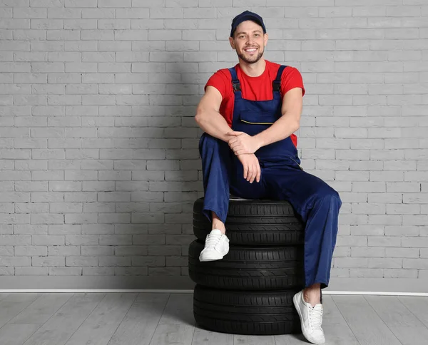 Masculino mecânico em uniforme com pneus de carro contra fundo de parede de tijolo — Fotografia de Stock