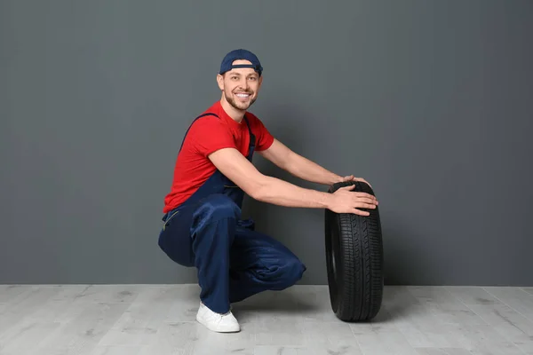 Mecânico masculino em uniforme com pneu de carro no fundo da parede cinza — Fotografia de Stock
