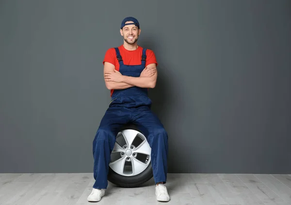 회색 벽 배경에 자동차 타이어와 유니폼에 남성 정비공 — 스톡 사진