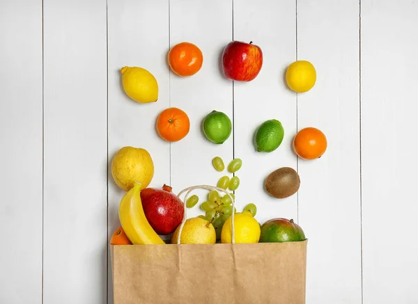 Papieren zak met vers tropisch fruit op witte houten achtergrond — Stockfoto