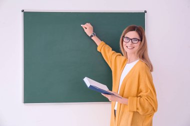 Genç kadın öğretmen sınıfta yazı tahtası üzerinde yazma