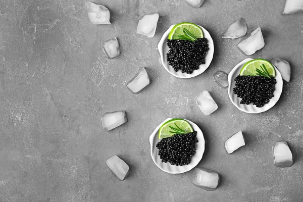 Placas con caviar negro y cubitos de hielo sobre fondo gris — Foto de Stock