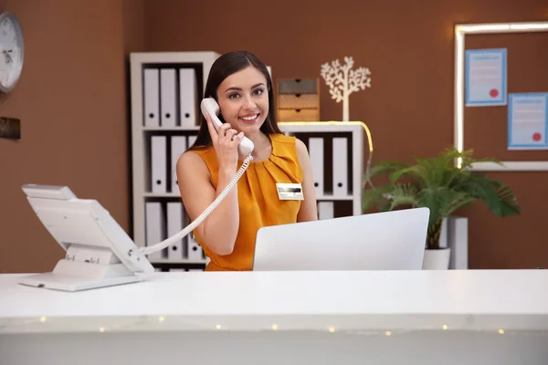 Женщина секретарша разговаривает по телефону на стойке регистрации отеля — стоковое фото