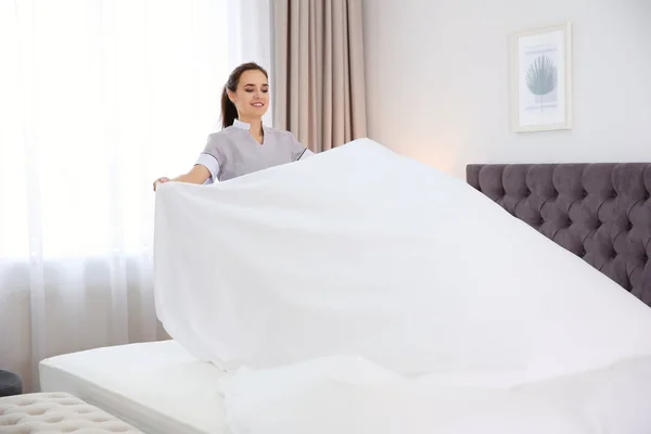 Jovem empregada fazendo cama no quarto do hotel — Fotografia de Stock