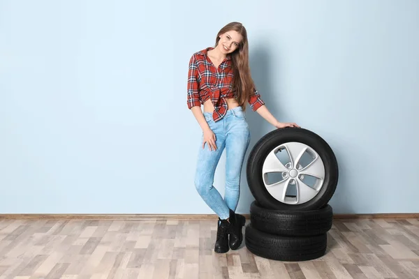 Mladá žena v svůdné oblečení s auto pneumatiky na šedou stěnu pozadí — Stock fotografie