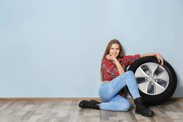 Jovem mulher em roupa sedutora com pneu de carro no fundo da parede cinza — Fotografia de Stock