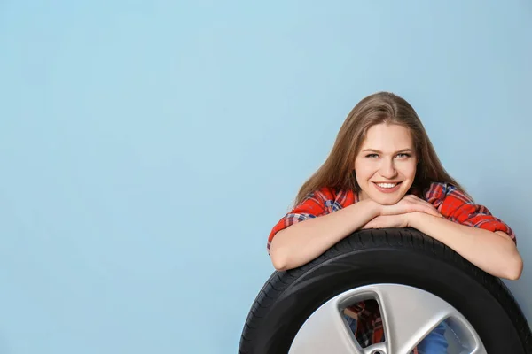 Jovem mulher em roupa sedutora com pneu de carro no fundo cinza — Fotografia de Stock