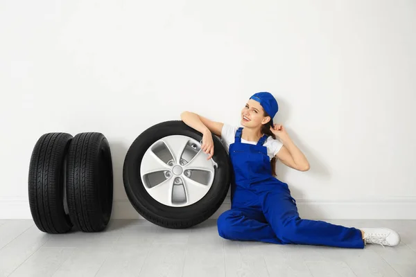 Mecânico feminino com pneus de carro no fundo da parede leve — Fotografia de Stock