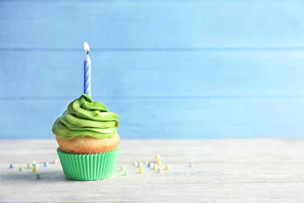 Heerlijke verjaardag cupcake met brandende kaars op tafel tegen een achtergrond met kleur — Stockfoto