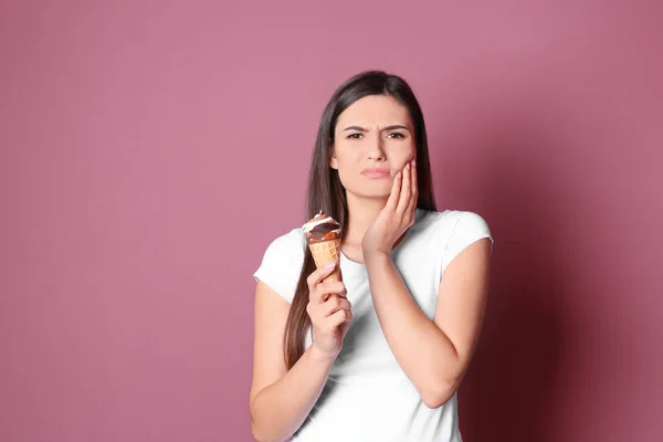 敏感な歯と色の背景上に冷たいアイスクリームを持つ若い女性 — ストック写真