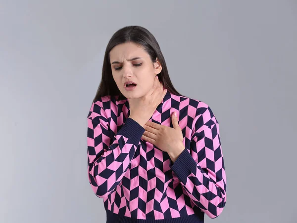 Jonge vrouw lijdt aan zere keel op lichte achtergrond — Stockfoto