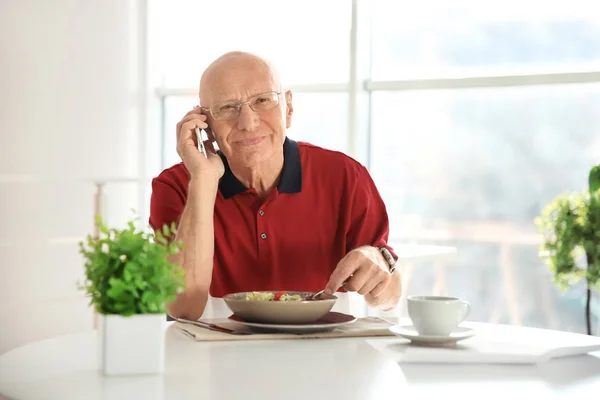 Anciano hablando por teléfono mientras desayuna en casa —  Fotos de Stock