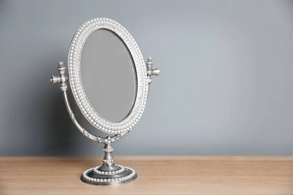 Elegantní zrcadlo na stole poblíž šedá stěna — Stock fotografie