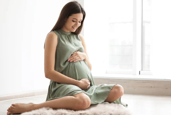 Νεαρή έγκυος γυναίκα που κάθεται στο πάτωμα κοντά στο παράθυρο στο σπίτι — Φωτογραφία Αρχείου