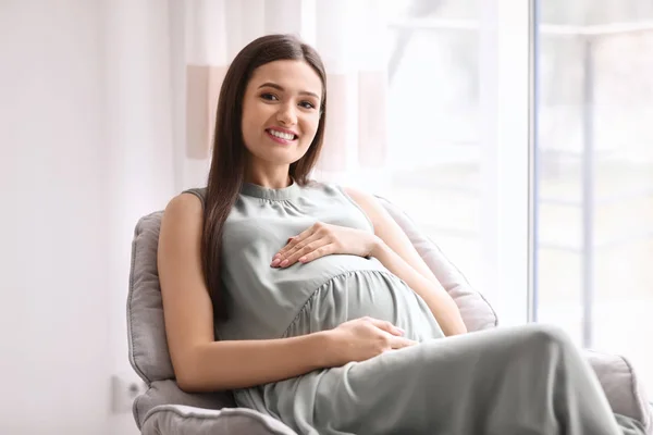 Νεαρή έγκυος γυναίκα που αναπαύεται στην πολυθρόνα στο σπίτι — Φωτογραφία Αρχείου
