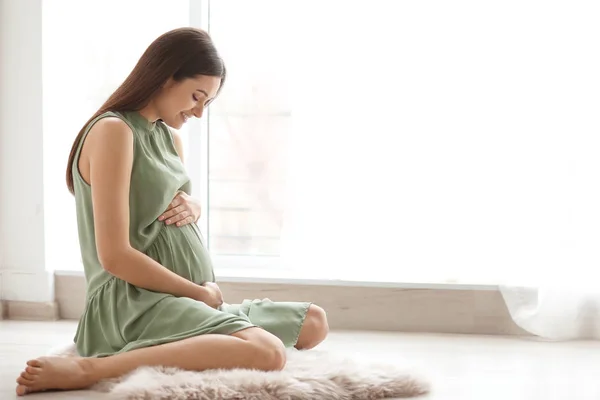 Młoda kobieta w ciąży, siedząc na podłodze w pobliżu okna w domu — Zdjęcie stockowe