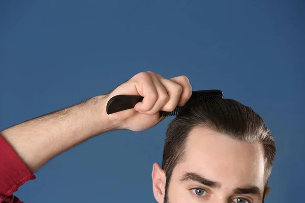 Portrait of young man combing his hair on grey background — Stock Photo, Image