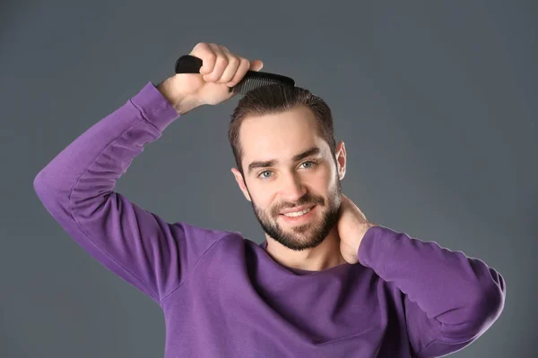 Портрет молодого чоловіка, що розчісує волосся на сірому фоні — стокове фото