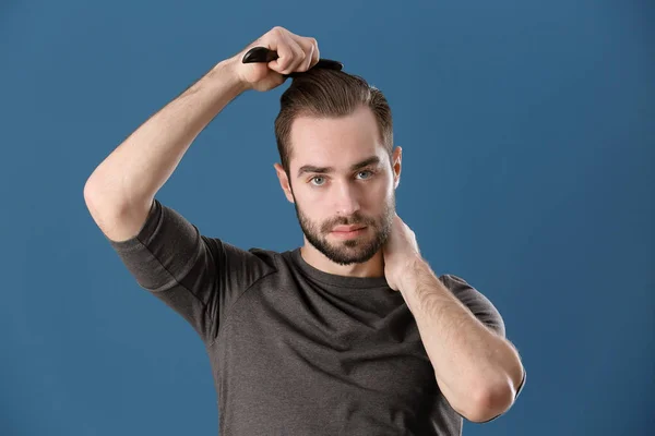 Portrait of young man combing his hair on color background — Stock Photo, Image
