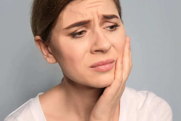 Młoda kobieta cierpiąca na ból zęba na szarym tle — Zdjęcie stockowe
