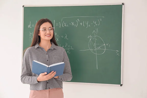 Professora com livro em pé perto de quadro negro em sala de aula — Fotografia de Stock