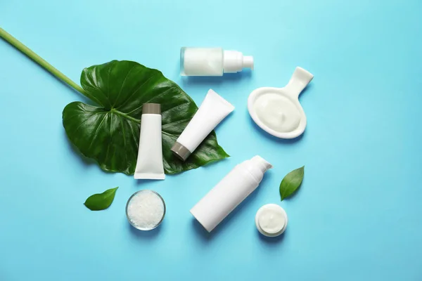 Farklı cilt bakımı kozmetik ürünleri renk arka plan, üstten görünüm üzerinde yeşil yaprakları ile — Stok fotoğraf