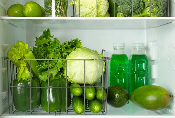 Different green vegetables and fruits on shelves of refrigerator — Stock Photo, Image