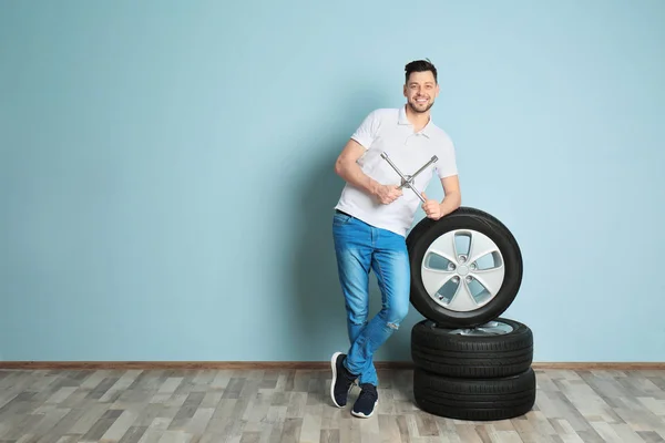 Mladý muž obeznámený s auto pneumatiky na barvu zdi pozadí — Stock fotografie