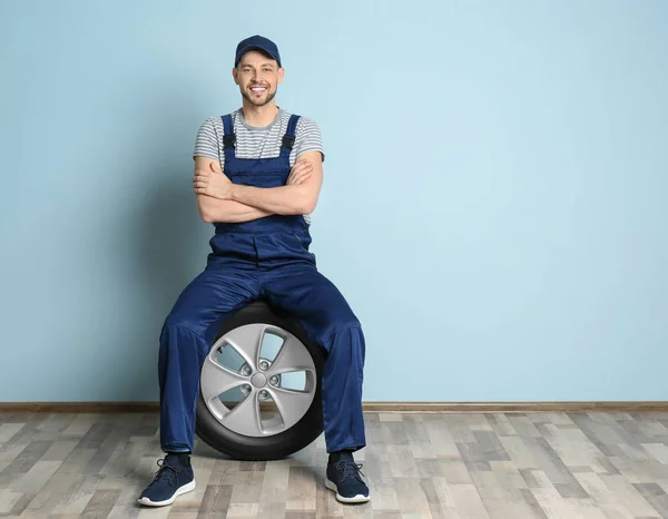 Mecánico masculino con neumático de coche en fondo de pared de color —  Fotos de Stock