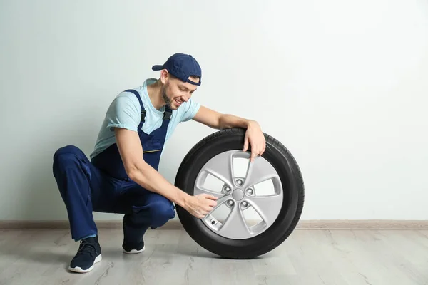 Mecânico masculino com pneu de carro no fundo da parede branca — Fotografia de Stock