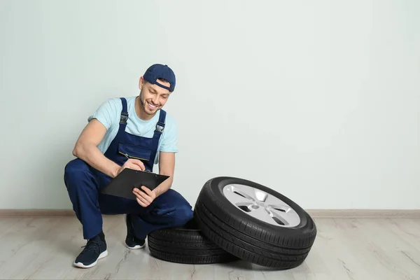 Mecânico masculino com pneus de carro no fundo da parede branca — Fotografia de Stock