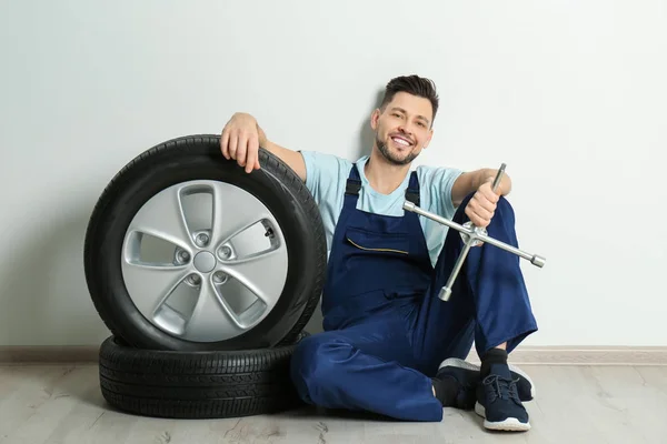 Mecánico masculino con neumáticos de coche sobre fondo blanco de la pared — Foto de Stock