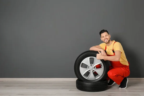 Mecânico masculino com pneus de carro no fundo da parede de cor — Fotografia de Stock