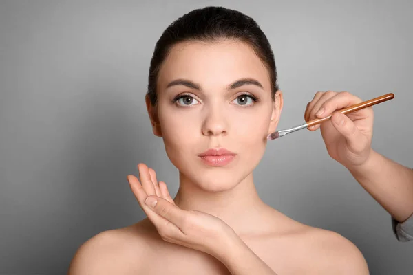 Artista Visage aplicando maquiagem no rosto da mulher contra fundo cinza. Produtos cosméticos profissionais — Fotografia de Stock