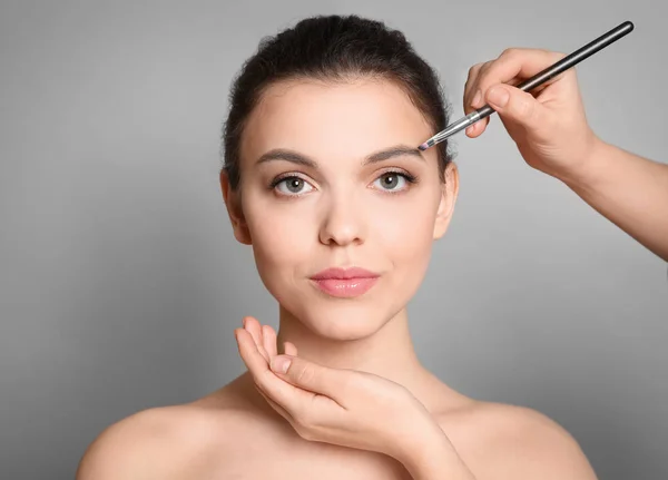 Visage konstnären tillämpa makeup på kvinnans ansikte mot grå bakgrund. Professionella kosmetiska produkter — Stockfoto