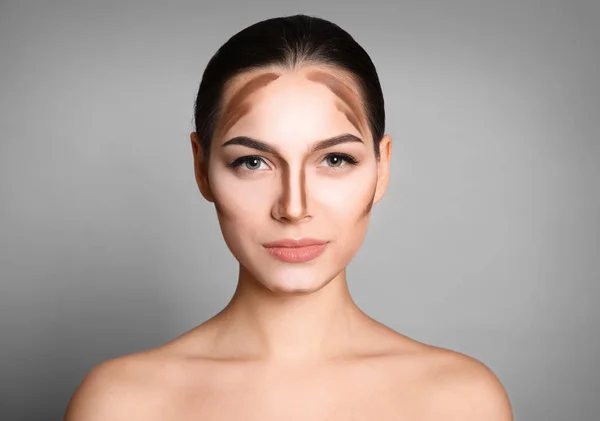 Ung kvinna med contouring linjer på hennes ansikte mot grå bakgrund. Professionell makeup produkter — Stockfoto