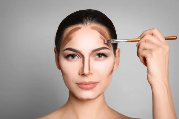 Ung kvinna applicera contouring linjer på grå bakgrund. Professionell makeup produkter — Stockfoto