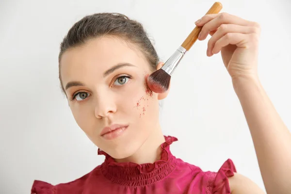 Mujer joven que aplica maquillaje sobre fondo claro. Productos cosméticos profesionales — Foto de Stock