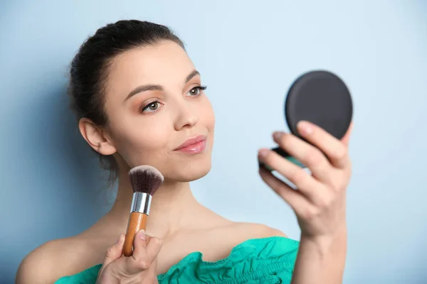 Ung kvinna tillämpa makeup på färgbakgrund. Professionella kosmetiska produkter — Stockfoto