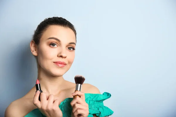 Jonge vrouw met lippenstift en make-up borstel op kleur achtergrond. Professionele cosmetica — Stockfoto