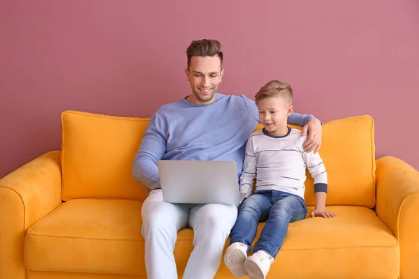 Jongetje en zijn vader met laptop zittend op de Bank, binnenshuis — Stockfoto